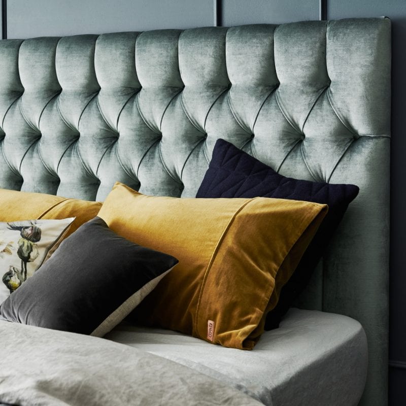 Diamond shaped deep-buttoned timber bedhead in crushed velvet styled in dark blue bedroom