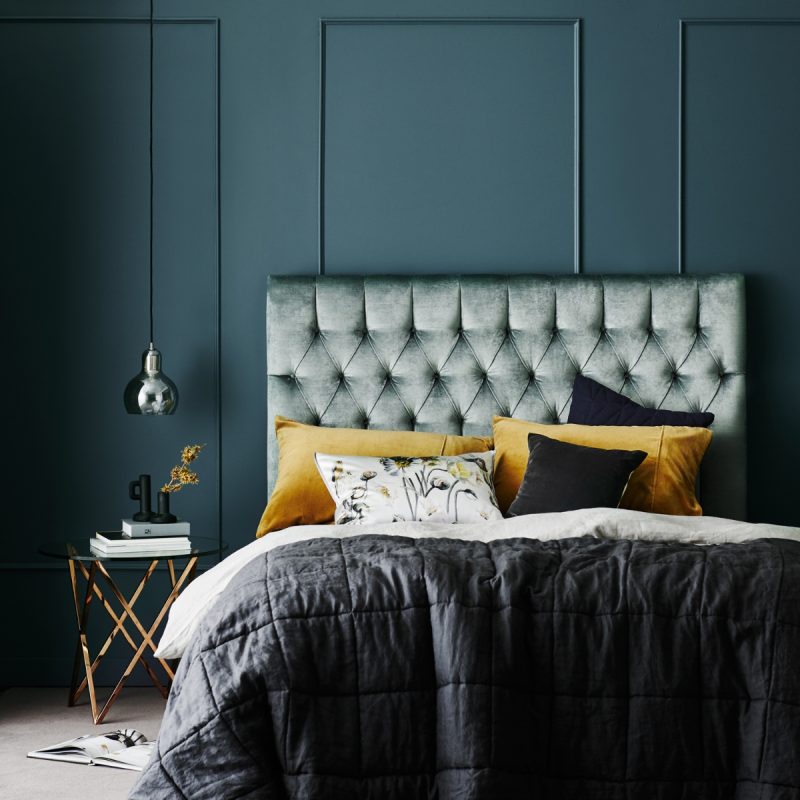 Deep-buttoned timber bedhead in crushed velvet styled in dark bedroom
