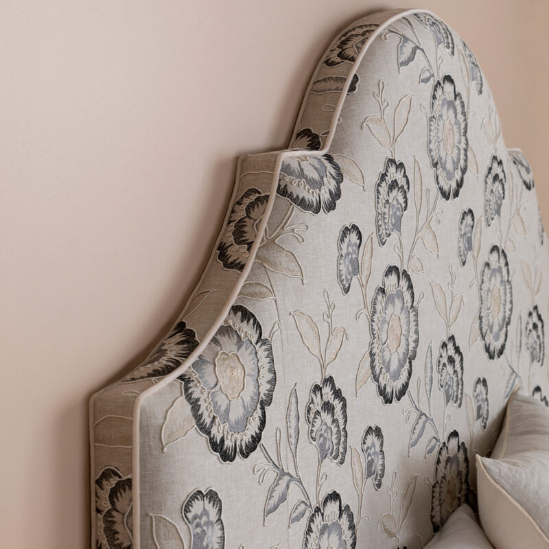 Close-up of a floral upholstered headboard featuring a floral pattern in shades of black, cream, and gray against a neutral wall.