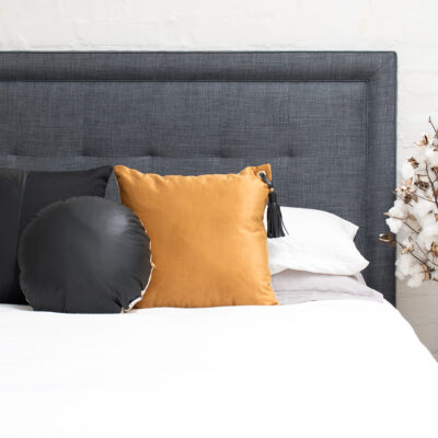 A cozy bed with a dark gray headboard, featuring a round black cushion, a mustard square pillow with a tassel, and cotton branches, conveying comfort and elegance.