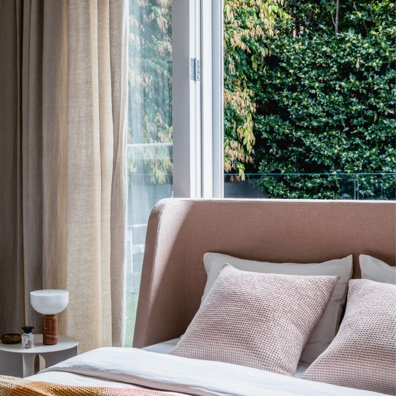 Layered master bedroom with dusty pink curved bedhead with marble side table. In a garden view bedroom