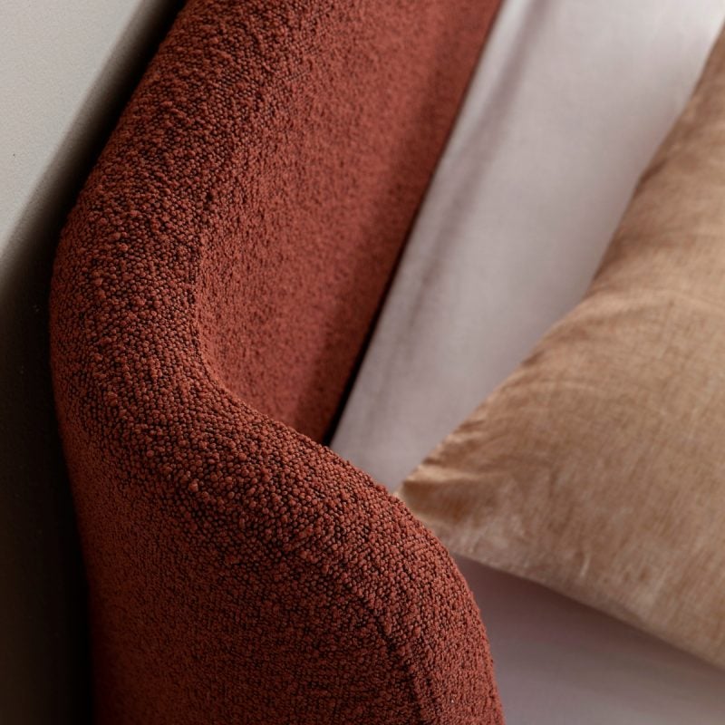Curved rust boucle bedhead with textured linen wrapping around bed