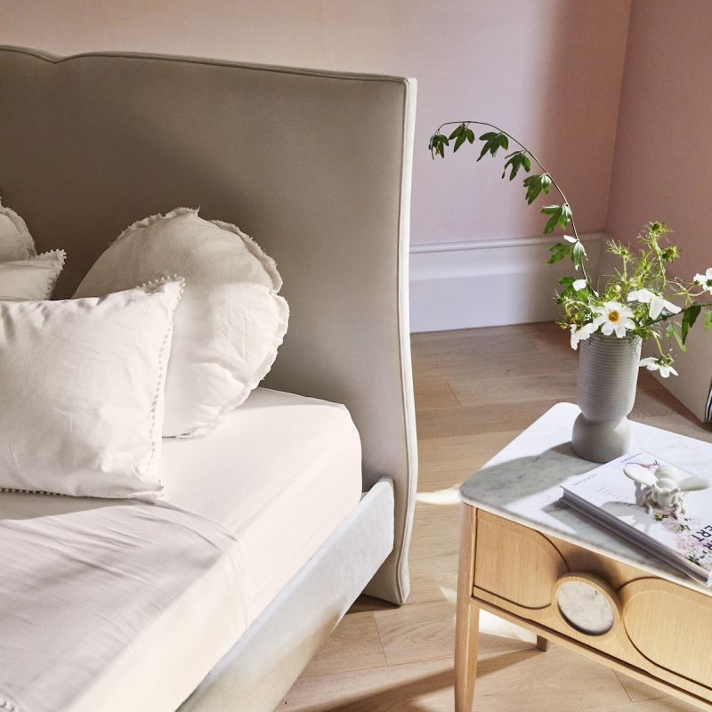 Grey velvet curved upholstered bed in pink room with fresh spring flowers